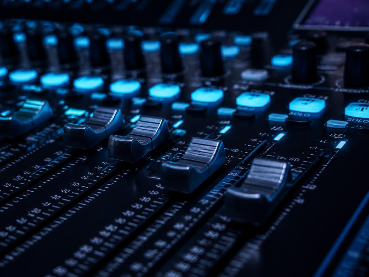 Professional audio mixing console faders lit with cyan indicators at a corporate event